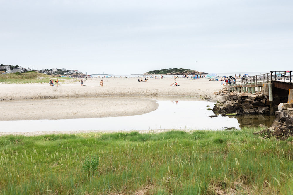 Good Harbor beach photograph scene with people walking along the shore and a wooden dock extending into the water.