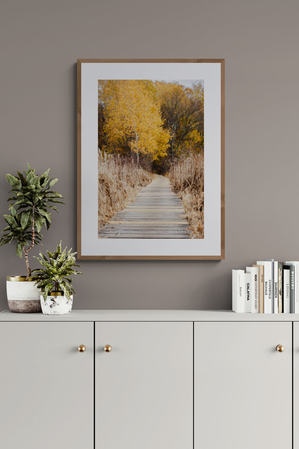 Framed photograph of a boardwalk with autumn trees as wall art in a living room.
