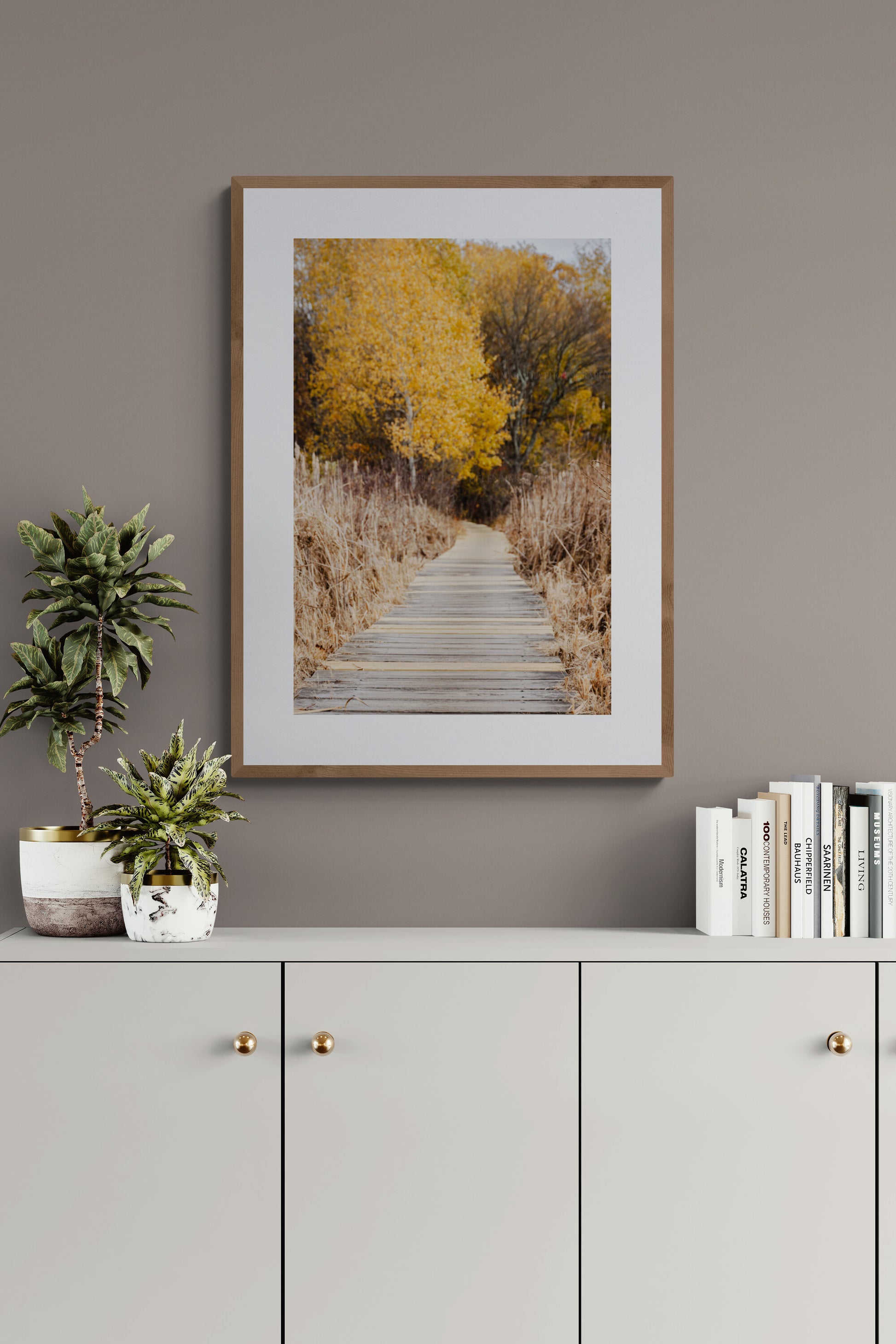Framed photograph of a boardwalk with autumn trees as wall art in a living room.